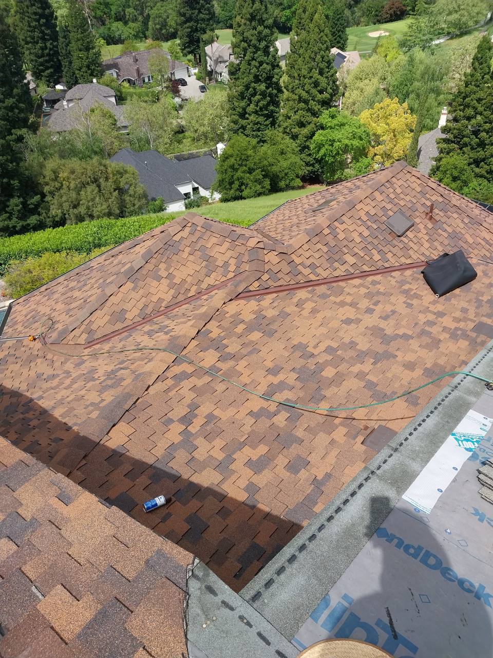 Wide aerial view of finished multi-tone dark brown shake-style roof with hillside golf course in the distance